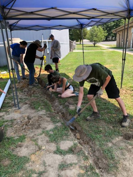 using a pickaxe to dig a trench for a rain garden at indian avenue school